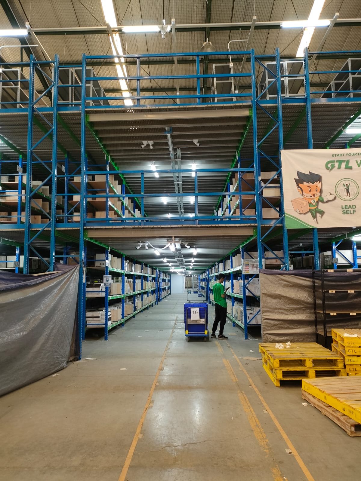 Aisle rak gudang FMCG bertingkat dengan mezzanine di atasnya