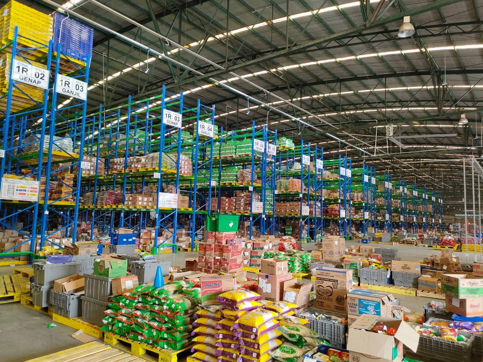 Rak gudang FMCG penuh karton dan sak produk consumer goods
